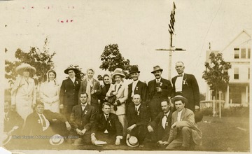 A group portrait of dressed up men and women posed in front of a white house.