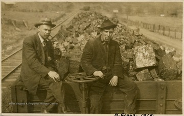Men are sitting on the front of a coal car. Both men are wearing hats and smoking pipes. The man on the right is identified as Mr. H. Groos.