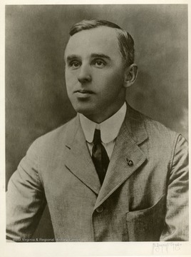 Unidentified man in light suit, white shirt, and black tie. "X" button on his lapel.