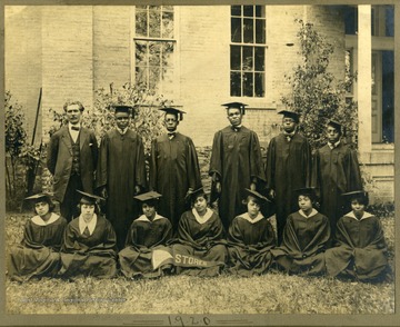 Class of 1920 in caps and gowns near a building at Storer College. First Row: Pres. McDonald, Harris, Clark, Lee, Walker, Redman. Second Row: Paker, Freeman, Arrington, Snowden, Harmon, Scott, Wildy.
