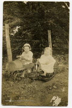 Photograph postcard of two small children, one riding a pedal car and one on a rocking horse. Information included with the photograph, "From Wookie and Woodrow Formish" and "Names ... looked up Ancestry.com..." The card is addressed to Mrs. Nada Godfrey, Bobbin, W. Va.