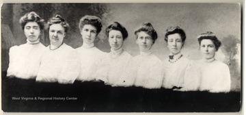 The Spinster Club at Lucy Wood Lawrence's wedding, February 18, 1908. From left: Bess Brown, Willa Brand, Sallie Bennett, Lucy Wood, Minnie Core, Josie Kunkle, Tillie Bernhardt. The Spinster Club of Morgantown flourished by the first decade of this century. At least two members married. All were Morgantowners who had graduated from high school and several had finished West Virginia University. Most were teachers. The Club met to socialize and visit on Saturday nights, with an occasional male friend or fiance allowed to attend. Members helped Ruth Wood, a pioneer stenographer, Realtor,and political candidate, raise her sister Lucy's daughter after Lucy died in China giving birth to her only child.