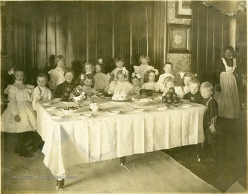 Several well dressed children gathered around a set dining room table with a birthday cake; Margaret Gibson is the little girl standing behind the cake