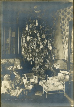 Margaret, daughter of Braxton D. Gibson and Mary Mason Gibson, is sitting among her dolls and toys, wearing a head dress.