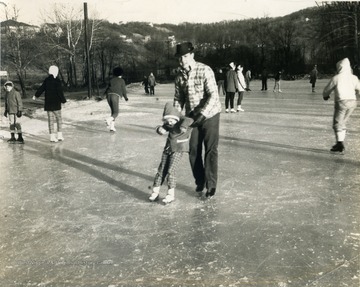 Unidentified little girl gets help ice skating from unidentified man.