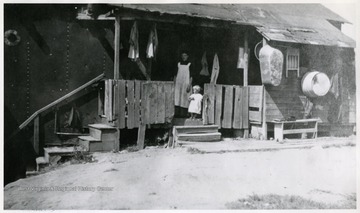 Located on Long Alley, 4 room tar paper structure with unidentified woman and child standing on the porch. 