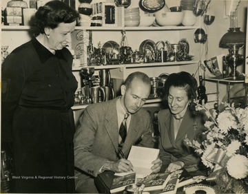 Mystery writers, George and Kay Evans of Preston County, West Virginia autograph a copy of their book, "Never Wake A Dead Man" for Mrs. Arthur Dunn.