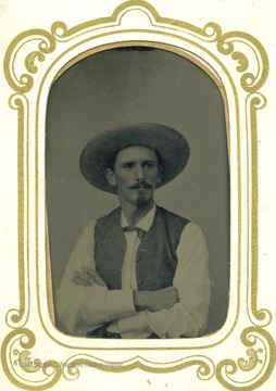 Unidentified man wearing a large hat, vest, goatee and mustache. The tintype is encased in a small glass frame. 