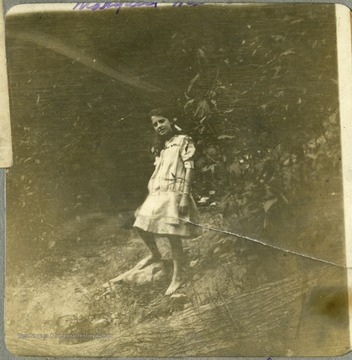 Barefoot little girl, Margaret Mathers standing in a wooded area.