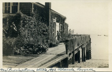 Post card photograph of artist Blanche Lazzell watering her flowers in front of her studio which is on a pier in Provincetown, Massachusetts located on Cape Cod.