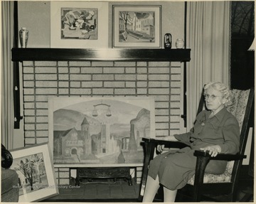 Blanche Lazzell sits in her family's living room with a few of her paintings. The painting on the floor, far left is E. Moore Hall and Stewart Hall on the West Virginia University campus.
