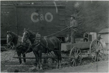 Unidentified teamster holds the reins of a team of horses, while standing in an empty wagon parked alongside a C &amp; O railroad car. The photograph was possibly taken at a depot in Summers County. 