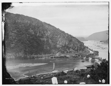 Maryland, the Chesapeake &amp; Ohio Canal and a reconstructed Baltimore and Ohio Railroad bridge on the Potomac River as viewed from the Harpers Ferry cemetery. Note the head stones in the foreground and the smoke stack of the burned out United States Armory below. The photograph was taken during the Civil War.
