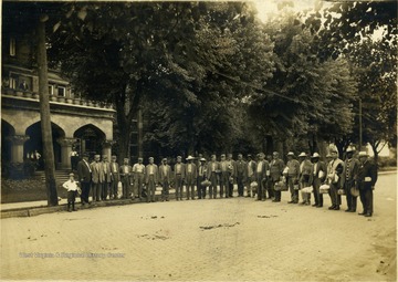 Group portrait of several unidentified inmates standing on a brick paved street on the state prison grounds. Two men standing at each end, wearing suits, are probably staff. None of the subjects are identified.