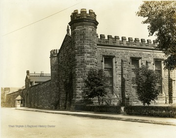 View of a corner of the complex of the state prison, with the front building in the foreground and the small wooden guardhouse next to the five foot thick wall.