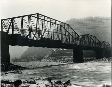 Photograph was taken along the river bank, looking up at the bridge as two locomotives pass each other.