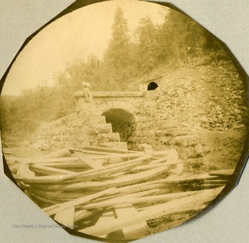 Unidentified man sitting on top of a culvert. Several supports use to shape the culvert are lying in the foreground. This image is probably a pinpoint photograph.