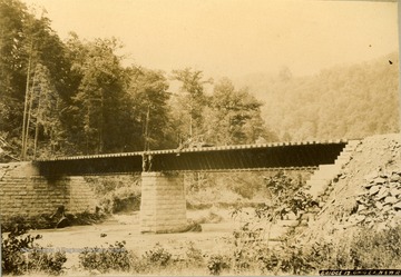 Two unidentified individuals are standing on the middle pier and two are sitting on the bridge and a hand-car.