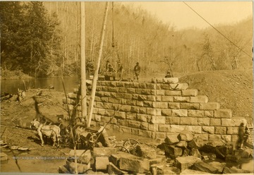 Unidentified workers use a pulley to move huge blocks of stone during the building of a bridge on the Norfolk and Western Railroad.