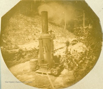 Unidentified worker stands next to an engine run by steam.