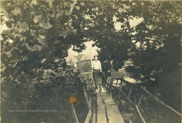 Unidentified man stands on a wooden, plank bridge crossing Hans Creek.