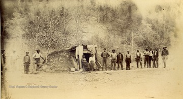 Several unidentified black workers and two women pose outside the entrance to what is possibly a dwelling built into the side of a hill. The photo was taken during the construction of the Ohio extension of the Norfolk &amp; Western Railroad.
