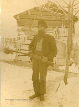 Hatfield stands in the snow with a rifle in hand outside a cabin. The photo was taken during construction of the Ohio extension of the Norfolk & Western railroad.