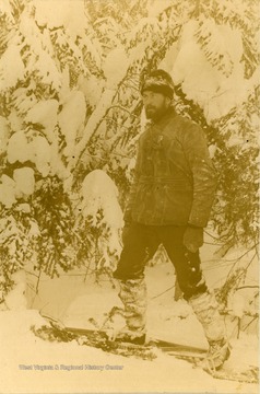 Unidentified bearded men makes his way through heavy mountain snow, wearing snow shoes. The photograph was taken during the construction of the Ohio extension of the Norfolk &amp; Western Railroad.
