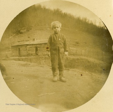 Unidentified boy wearing boots and an unhappy expression for the camera. The photograph was taken during the construction of the Ohio extension of the Norfolk &amp; Western Railroad in southern West Virginia.