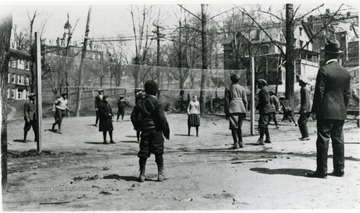 Several African-American children playing in the school yard. Beechurst was a segregated school. Martin Hall on the WVU campus is seen in the background. All persons in the photo are unidentified. Information on p. 114 in "Our Monongalia" by Connie Park Rice. Information with the photograph includes "Reproduced from the John H. Hunt family photos, held by WVU Women's Centenary Project, Center for Women's Study Archive. Original Loaned by Virginia Hunt Chandler. 