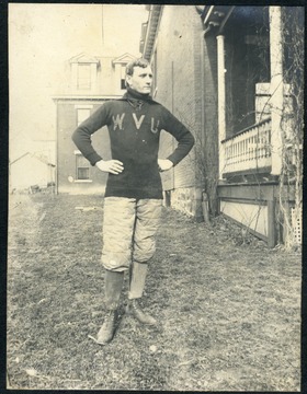 Unidentified WVU student wearing a football uniform, with large "WVU" across his chest and shin guards with high-top shoes.