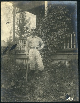 Unidentified student, wearing a baseball uniform with "WVU" embossed on the shirt, poses with a bat.