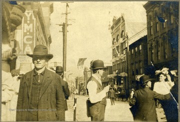 YMCA (Young Men's Christian Association) sign on the left side, behind a man wearing large hat. All persons in the photograph are unidentified. 