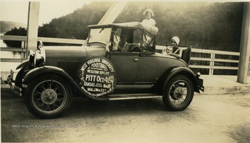 Automobile, parked on a bridge with a WVU football schedule displayed on the driver's door. Subjects in the photograph: Susie Squires Hill in the passenger's seat, her daughter Colleen D. Hill behind the passenger seat and her infant daughter Jo Ann Hill in the backseat. The woman holding Jo Ann is unidentified. The Pitt game appears to be the most important given the large print.  