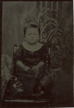 Toddler sitting in a chair, holding a purse.