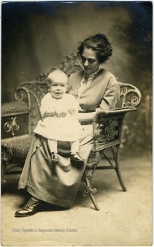Postcard photograph of an unidentified woman holding an infant in her lap. 