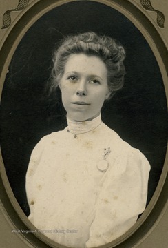 A young woman in a high neck white dress. She appears to be wearing both a necklace and a pin watch. 