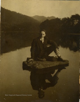 Dapperly dressed in a suit, O'Rourke poses, sitting on rock in the river.