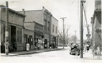 Postcard photograph of several people walking along a street in downtown Belington. All persons in this photograph are unidentified. 