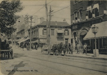 This laminated postcard image of downtown Morgantown shows horse-drawn wagons and streetcar tracks in the brick paved street.