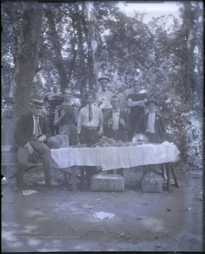 Several unidentified young men, some wearing swim suits pose around a picnic table.