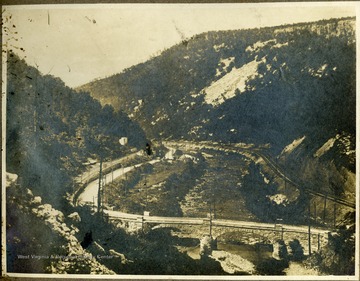 Stone railroad bridge crosses a small river in a mountain valley.