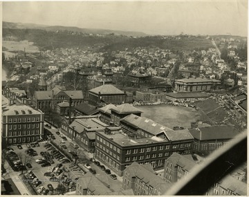 View of the main downtown campus in the foreground includes Mechanical Hall II, Stewart Hall and Commencement Hall also known as Reynolds Hall. In the center, behind Chitwood Hall is old Mountaineer Field and to the far left is the steel beam foundation of Armstrong Hall under construction. Upper,right corner of the photograph, on the top of the hill is the Morgantown Country Club where the College of Law is now located.