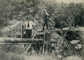 Fred S. Hathaway and unknown person walking oil pipeline.