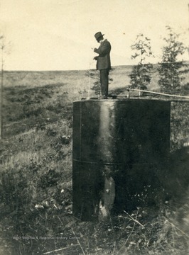 Fred S. Hathaway on top of an oil tank loacted on Dr. W. T. W. Dye's farm.