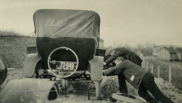 Two men change a tire on a Model T Ford.