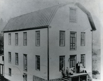 This picture was taken before 1917 as the mill was painted red in 1917. Boss Park bought this mill in 1907 and move there from Tyler County, West Virginia. He modernized the equipment. Boss Park and his wife Mary are standing at the right of the door. The child Mrs. Park is holding is Harry or Earl. Mae Howard, wife of Will Howard is standing on steps just beyond Mrs. Park. Children left to right: Clarence Howard, Ethel Park, Frank Park- in front sitting. Photo labeled: Sara Scott