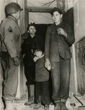 Caption on back of photo reads: "German civilians from the small farming community of Tenholz are received by an American soldier in a shattered house serving as a reception center in Lovenich. The 102nd Infantry Division of the Ninth U.S. Army captured Lovenich February 25, 1945."