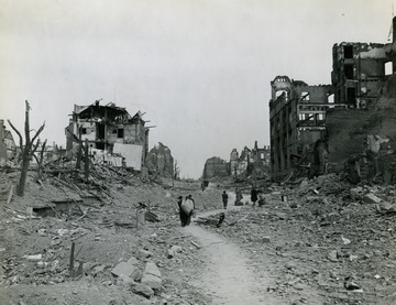 Caption on back reads "Civilians of Plauen, Germany, make their way through rubble filled streets in search of what articles they can salvage from their wrecked homes and shops. The city was captured by the 3rd U.S. Army following a devastating attack by Allied bombers."