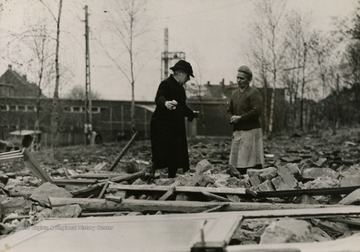 Caption on back of photo reads: "German woman (left) stands before the wreckage of her home and explains to a neighbor how a heavy Nazi shell leveled the building. Several civilians were injured by the enemy action against the town after its capture by American troops."